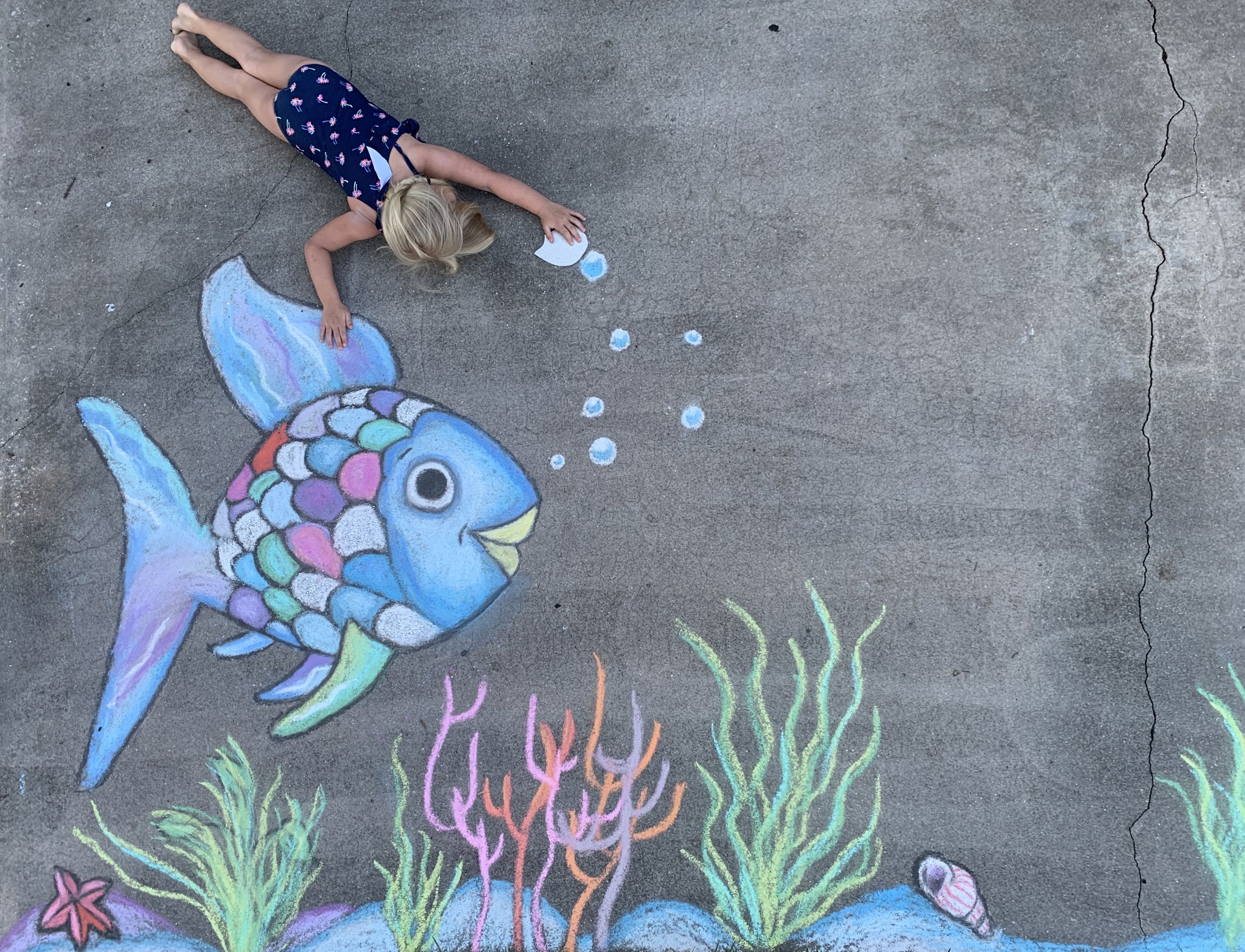 Child drawing a fish on the sidewalk